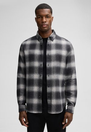 Gray and black checkered flannel shirt with button closure and a spread collar, worn over a black top, smooth texture and long sleeves.