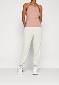 Ljusrosa ärmlös topp med smala remmar, kombinerad med krämfärgade joggers med sidostripes och elastiska muddar. Vita sportskor.