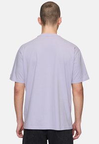 Camiseta de algodón lavanda con mangas cortas, cuello redondo y corte relajado. Textura suave, sin patrones ni accesorios visibles.
