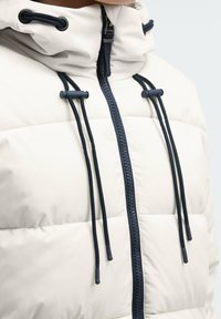 Gepolsterte weiße Jacke mit hohem Kragen, marineblauem Reißverschluss und verstellbaren Kordeln. Glatte Textur und gestepptes Muster mit marineblauen Akzenten.