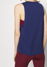 Top senza maniche blu navy con una vestibilità comoda, caratterizzato da un collo rotondo e spacchi laterali, abbinato a leggins bordeaux. Tessuto morbido e texturizzato.