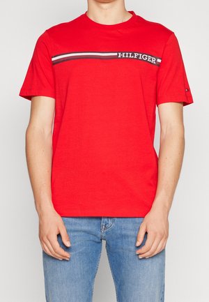 Punainen puuvillapaita lyhyellä hihalla. Aikaansaannoksena vaakasuora raitakuosi tummansinisestä ja valkoisesta rinnassa, johon on merkitty "HILFIGER."