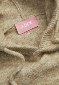 Maglione beige a maglia con una texture morbida, dotato di un colletto ripiegato e un'etichetta di tessuto rosa con la scritta "JJXX."