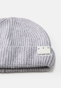 Gorro cinza tricotado com textura canelada, com a barra dobrada e um rótulo branco apresentando "CPH STUDIOS" em letras pretas.