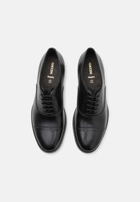 Zapatos de vestir de cuero negro con un acabado suave, diseño con cordones, detalles de costura sutiles, punta redonda y plantilla con marca.