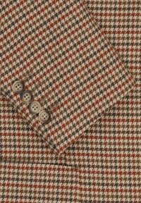 Tkanina z wełny w kolorze brązowym, beżowym i czerwonym w wzór houndstooth. Cztery okrągłe, neutralne guziki na mankiecie dodają szczegółu.