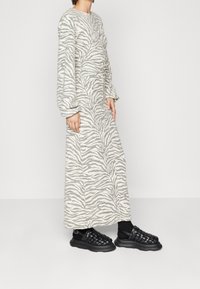 Długa, beżowa sukienka w wzór zebry z obszernymi rękawami. Połączona z czarnymi, plecionymi butami wsuwanymi z masywną podeszwą.