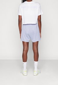 Bílý krátký top s fialovým nápisem "NIKE PRO." Doplněný světle fialovými šortkami s volným střihem a elastickým pasem.