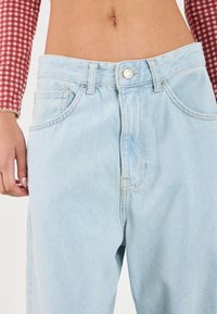 Ljusblå denimjeans med hög midja, avslappnad passform, framfickor och silverfärgad knäppning. Mjuk textur och blekt utseende.