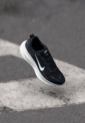 Black and white Nike running shoe suspended above asphalt ground with white painted markings.