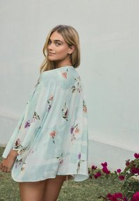 Cvjetni kimono-stil pokrivač u svijetlo plavoj boji, s pastelnim uzorcima cvijeća, lepršavim materijalom i otvorenim rukavima. Idealno za slojevito nošenje.