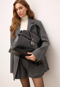 Melnas ādas rokas soma ar strukturētu formu, sudraba aksesuāriem un noņemamu siksnu. Ispējš top rokturiem un elegantu dizainu.