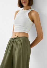 Bílý žebrovaný crop top s vysokým výstřihem, kombinovaný se zeleno-olivovými, texturovanými, volně padnoucími kalhotami s elastickým pasem a bočními kapsami.