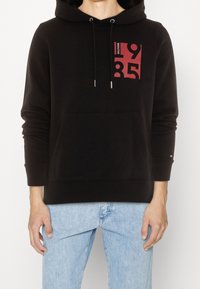 Felpa nera con cappuccio, caratterizzata da un design grafico rosso sul davanti, con laccetti, tasca frontale e polsini a coste.