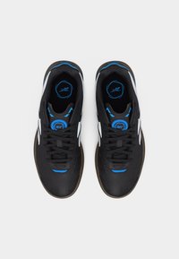 Ζευγάρι μαύρα αθλητικά παπούτσια με λευκές λεπτομέρειες στα πλάγια, μπλε τόνους και καφέ σόλες, σε θέα από πάνω σε λευκό φόντο.