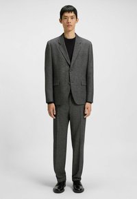 Gray tailored suit made of textured fabric, featuring a notched lapel jacket with two buttons and flat-front trousers, worn over a black top.