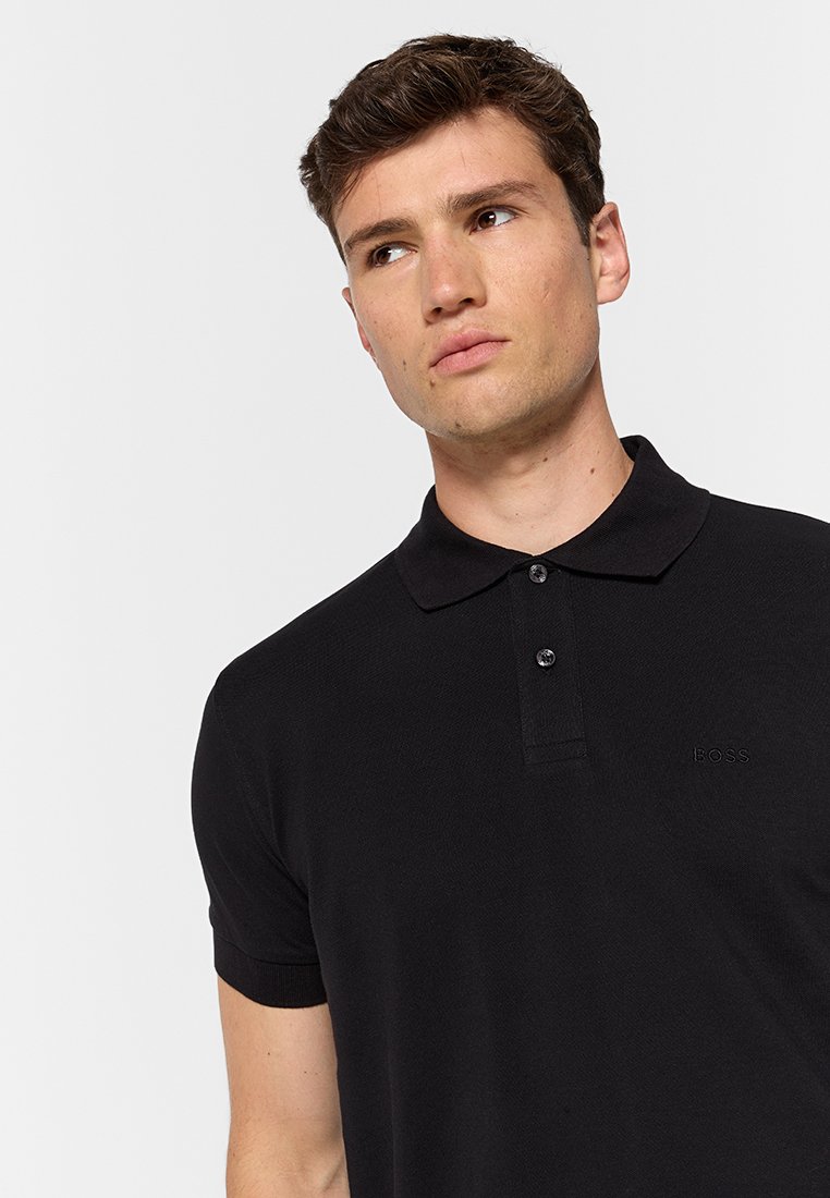 Polo noir en coton texturé avec un col classique, patte de boutonnage à trois boutons et broderie de logo discrète sur la poitrine.