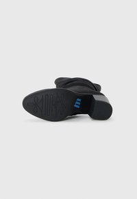Schwarze Knöchelstiefel mit einem texturierten Stoff-Obermaterial, Blockabsatz und Gummisohle, die ein blaues Logo und ein dekoratives Muster auf der Sohle aufweist.
