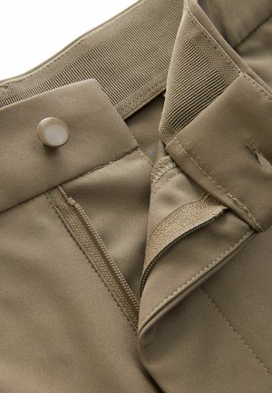 Beige kangast lühikesed püksid, millel on nööp ja lukukinnitus, tugevdatud vöökoht ja sile tekstuur. Õmbluste detailid on nähtavad.