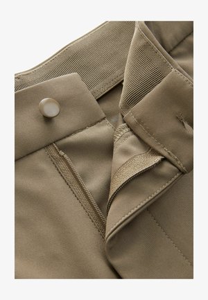 Beżowe krótkie spodenki z tkaniny z zapięciem na guzik i zamek błyskawiczny, posiadające wzmocniony pas i gładką teksturę. Widoczne detale szycia.