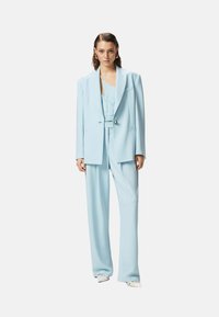 Completo su misura blu chiaro composto da giacca doppiopetto e pantaloni a gamba larga, realizzato in un tessuto liscio con una leggera lucentezza.