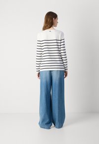 Langarm gestreept shirt in wit en marineblauw, gecombineerd met wijduitlopende lichtblauwe jeans. Zachte katoen stof met een ontspannen pasvorm en ronde halslijn.