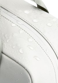 Borsa impermeabile bianca con gocce d'acqua sulla superficie, caratterizzata da una texture liscia, una forma curva e una tracolla grigia. Design minimalista con linee pulite.