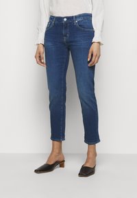 Mörkblå denimjeans med slim fit, ankellängd, femfickdesign och subtil blekning. Matchad med svarta öppna mule-skor.