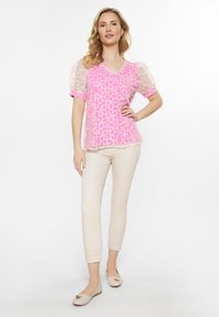 Lyserød blomsterlacemønster top med pufærmer, parret med beige ankel-lange bukser og lyse ballet flats med en dekorativ detalje.