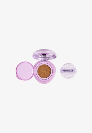Fond de teint compact cushion lilas avec une éponge à maquillage marron à l’intérieur, à côté d’un applicateur tampon à motifs étiqueté "Revolution."