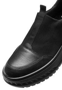Los zapatos negros tipo slip-on presentan una puntera de piel lisa y una parte superior de tejido texturizado, con paneles laterales elásticos y una suela gruesa y con diseño.