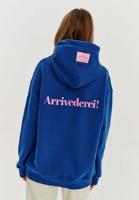 Modrá mikina s kapucí se velkým růžovým textem "Arrivederci!" na zadní straně. Obsahuje klokaní kapsu a růžovou značkovou nášivku na kapuci.