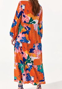 Maxiklänning i livlig orange med abstrakta, flerfärgade blommönster. Långa ärmar, lagerdesign och volangnederdel. Mjuk tygkvalitet.