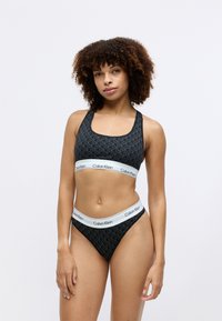 Svart sportsbh og matchende bikini med geometrisk mønster, med en hvit kant merket "Calvin Klein." Glatt stoff og tettsittende design.
