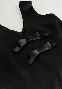 Schwarzes Satinbekleidungsstück mit tiefem V-Ausschnitt und zwei dekorativen schwarzen Schleifen vorne, das eine glatte und glänzende Textur zeigt.