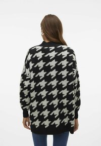 Svartvit houndstooth-mönstrad oversized tröja med ribbad halsringning och mudd, tillverkad av mjukt stickat material.