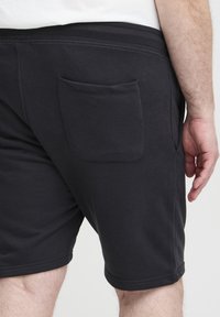 Black cotton shorts with a smooth texture, featuring a back pocket and elastic waistband. The design is simple with minimal stitching details.