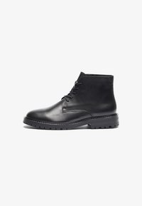 Botas de cuero negras hasta el tobillo con puntera redonda, cierre de cordones en la parte delantera y suela de goma texturizada con un patrón de relieve. Acabado suave, diseño minimalista.