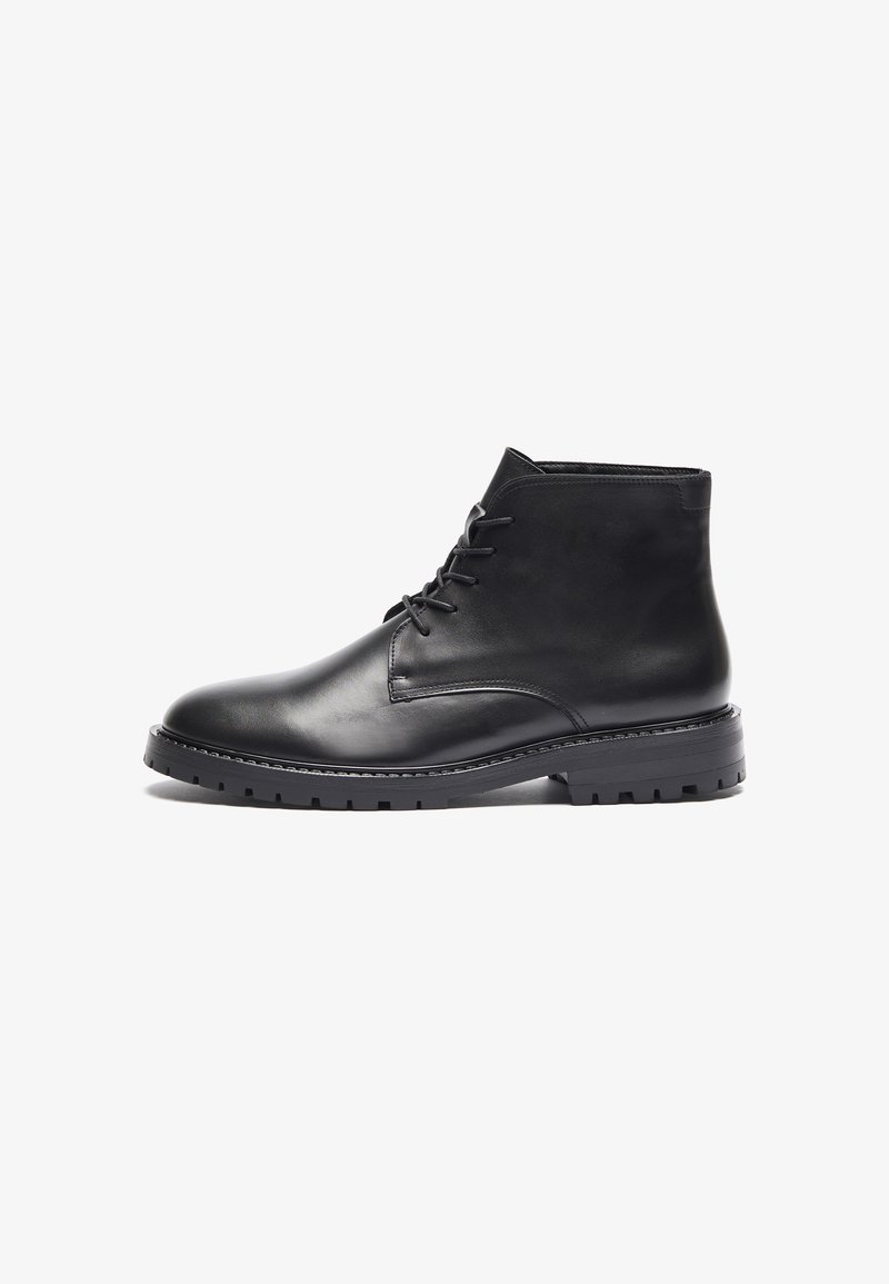 Botas de cuero negras hasta el tobillo con puntera redonda, cierre de cordones en la parte delantera y suela de goma texturizada con un patrón de relieve. Acabado suave, diseño minimalista.