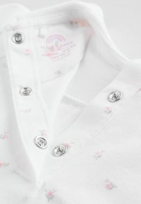 Hvid bomuldsheldragt med små blomsterprint, sølvfarvede trykknapper og rund halsudskæring. Blød tekstur og letvævet stof.