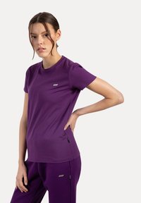 Camiseta de algodón morada con mangas cortas, cuello redondo y un sutil logotipo en el pecho. Textura suave con un diseño ajustado.