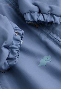Hellblaues Gewebe mit gerafften Ärmelbündchen; zeigt cartoonhafte Tiermuster in sanften Farben. Weiche Textur mit leichtem Glanz.