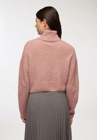 Zgniła różowa, krótka bluza z wysokim prążkowanym kołnierzem i opadającymi ramionami, w połączeniu z plisowaną szaro-skalną spódnicą, widziana z tyłu.