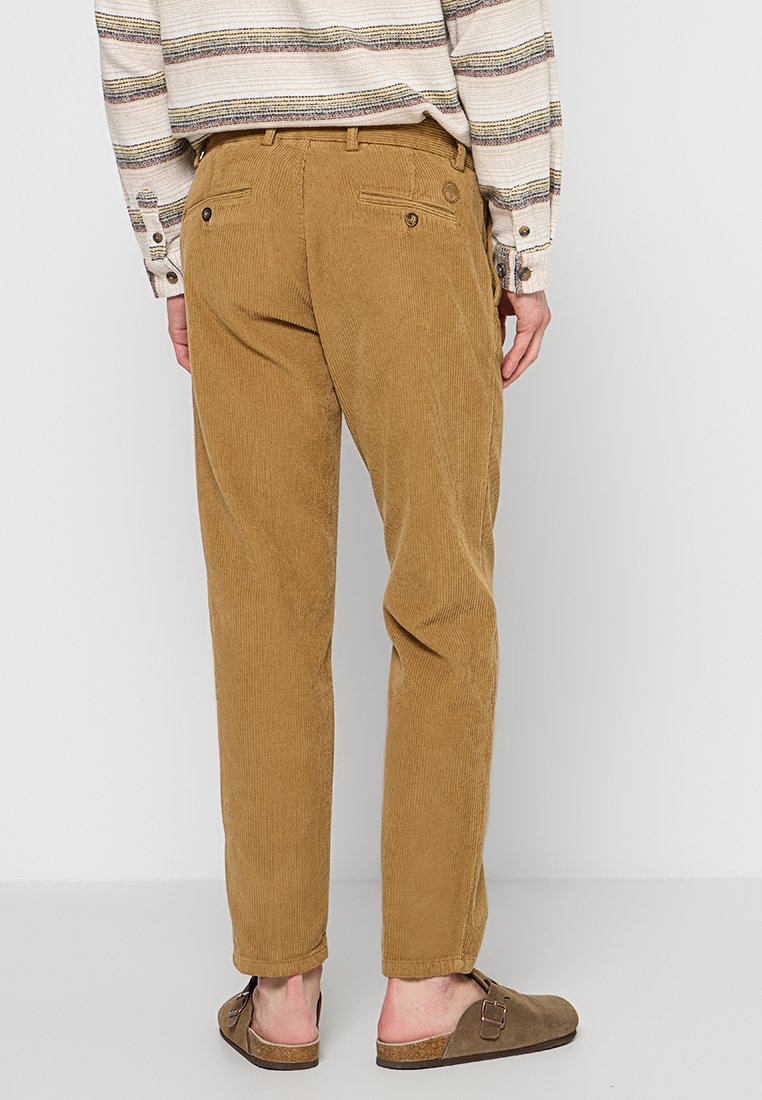 Pantaloni in velluto a coste di colore marrone chiaro con costole sottili; presentano due tasche posteriori con chiusura a bottone; indossati con un top a righe.