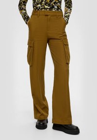 Cargo broek in mosterdgeel, met een recht model, twee zijzakken en een gladde textuur. G gedragen met zwarte plateau schoenen.