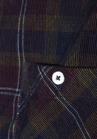 Kariertes Stoffmuster mit vertikalen und horizontalen Streifen in Marineblau, Burgunderrot und Senftönen. Beinhaltet einen weißen Knopf mit schwarzer Naht.