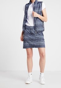 Kamizelka bez rękawów w marynarskim wzorze na białym polo, w połączeniu z granatową spódnicą i białymi butami sportowymi, z zamkiem błyskawicznym i teksturowanym materiałem.