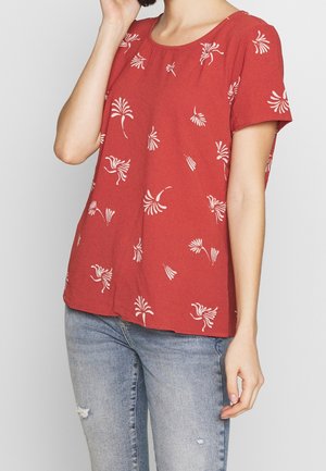 Top rosso a maniche corte con scollatura tonda, caratterizzato da un motivo floreale bianco, tessuto testurizzato e vestibilità morbida. Abbinato a jeans chiari strappati.