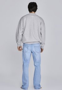 Pelēks svītra ar pārmērīgu piegriezumu un ribotas aproces, kā arī gaiši zili džinsi ar aizmugurējām kabatām un taisnas kājas dizainu.