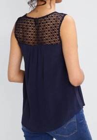 Granatowy top bez rękawów z kwiatową koronką na plecach, zaokrąglonym dołem i miękką teksturą. Odpowiedni do codziennego noszenia lub jako warstwa.